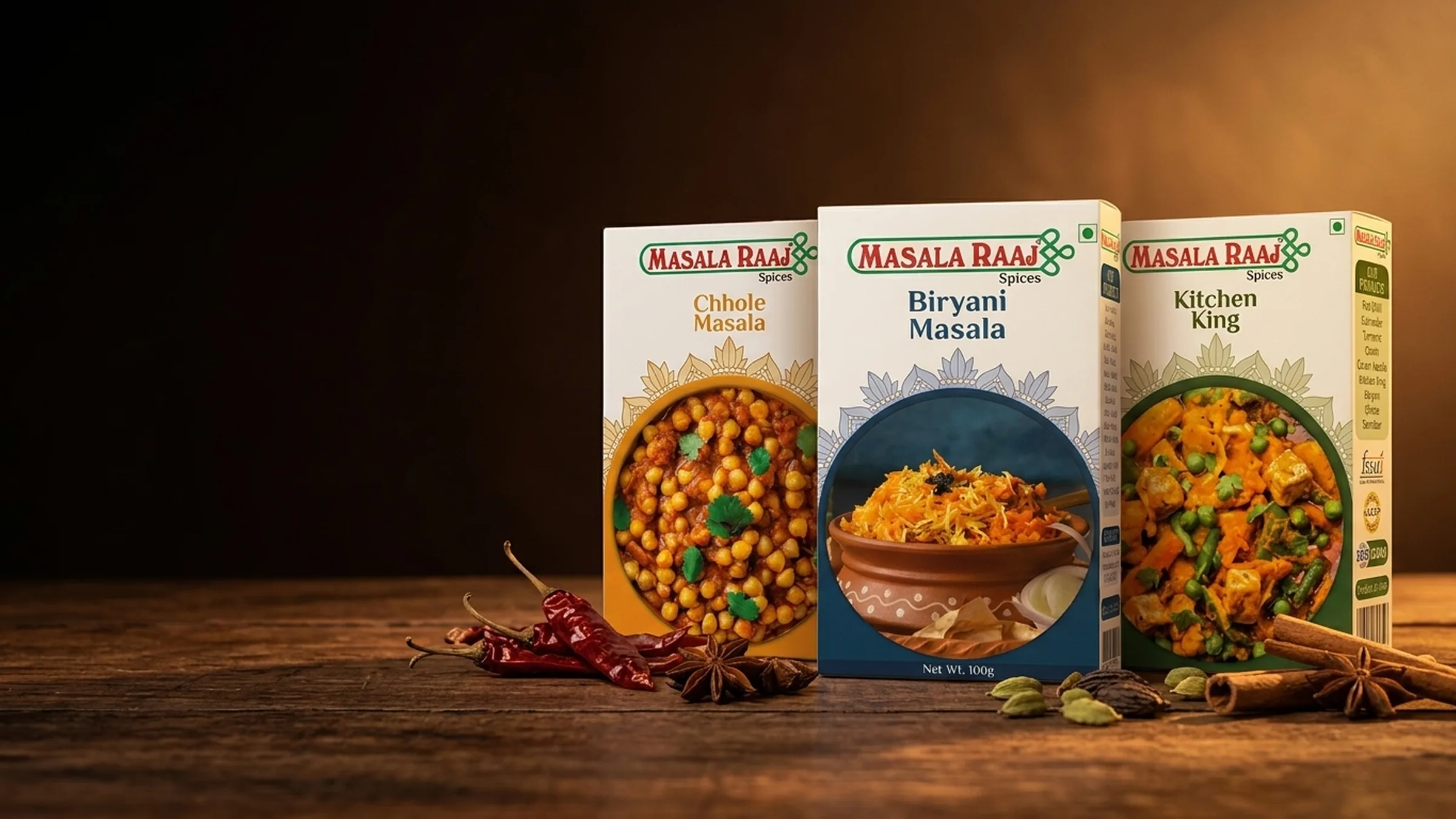 Masala Raaj blended masala cartons on a warm wooden table: Chhole Masala, Biryani Masala and Kitchen King, with dried chillies, star anise, cardamom and cinnamon